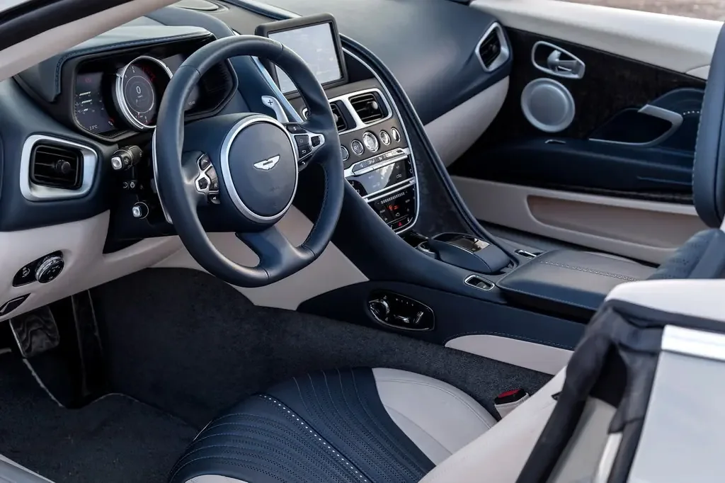 Фото Aston Martin DB11 (2023) — интерьер. Общий план салона: панель, консоль и передние кресла Aston Martin DB11 (2023) — интерьер