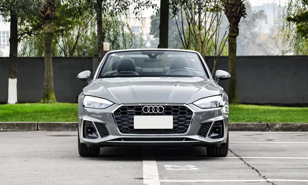 Фото Audi A5 (2024) — вид спереди, фото 3. Кузов в сером цвете: рисунок оптики и решётки задаёт узнаваемое «лицо» модели. Рисунок ходовых огней — подпись модели, по нему её узнают в потоке Audi A5 (2024) — вид спереди, фото 3