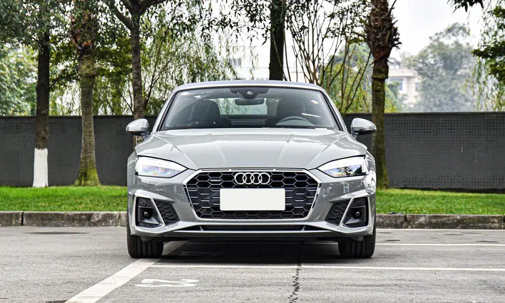 Фото Audi A5 (2024) — вид спереди, фото 7. Серый кузов, строгая симметрия оптики — базовый ракурс знакомства с дизайном. Дневные ходовые огни включаются автоматически с запуском Audi A5 (2024) — вид спереди, фото 7