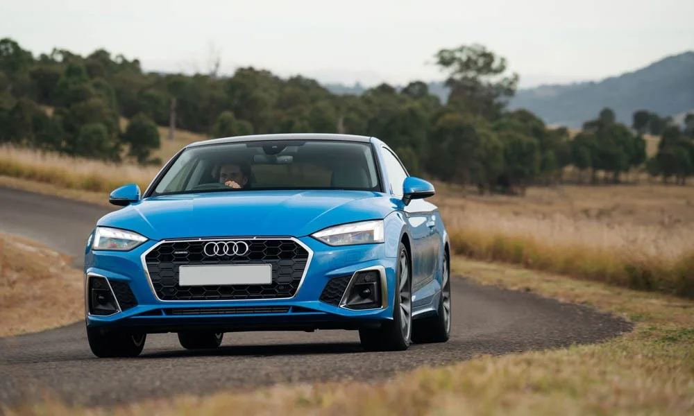 Фото Audi A5 — вид спереди, фото 19. Кузов в синем цвете: рисунок оптики и решётки задаёт узнаваемое «лицо» модели. Дневные ходовые огни включаются автоматически с запуском Audi A5 — вид спереди, фото 19