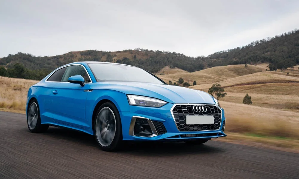 Фото Audi A5 — вид спереди, фото 20. Синий кузов, строгая симметрия оптики — базовый ракурс знакомства с дизайном. Рисунок ходовых огней — подпись модели, по нему её узнают в потоке Audi A5 — вид спереди, фото 20