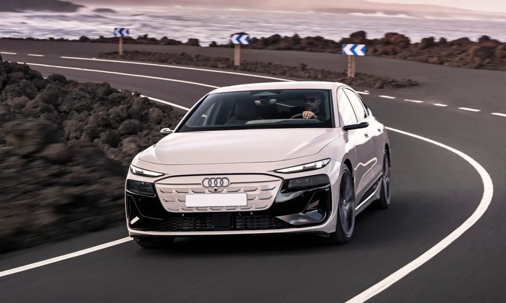 Фото Audi A6 Sportback e-tron (2024) — вид спереди, фото 4. Кузов в белом цвете: рисунок оптики и решётки задаёт узнаваемое «лицо» модели. Рисунок ходовых огней — подпись модели, по нему её узнают в потоке Audi A6 Sportback e-tron (2024) — вид спереди, фото 4