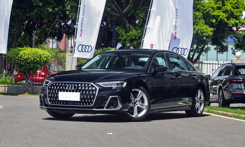 Фото Audi A8 L (2024) — вид спереди, фото 6. Передок в чёрном исполнении — крупная светотехника и выразительный бампер. Рисунок ходовых огней — подпись модели, по нему её узнают в потоке Audi A8 L (2024) — вид спереди, фото 6
