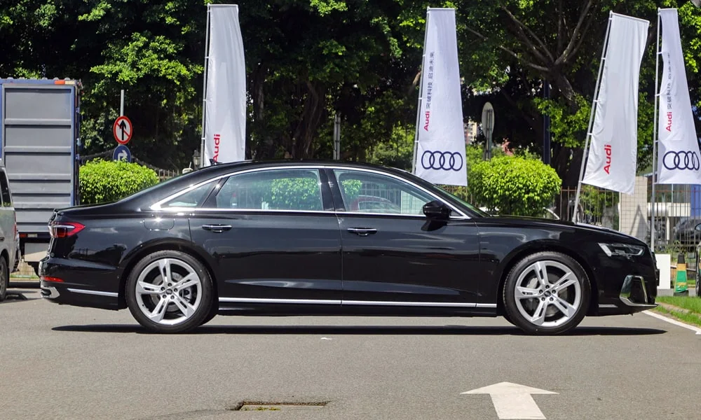 Фото Audi A8 L (2024) — вид сбоку, фото 3. Сбоку читаются линия остекления и характер выштамповок на чёрном кузове. Хромированные или чёрные молдинги окон отличают комплектации Audi A8 L (2024) — вид сбоку, фото 3