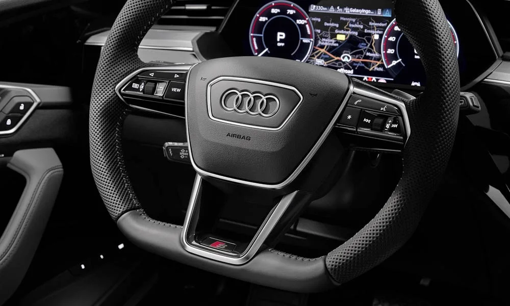 Фото Audi e-tron S — руль. Обшивка обода и компоновка спиц крупным планом. Клавиши на спицах управляют медиа, круизом и ассистентами — руки остаются на руле Audi e-tron S — руль