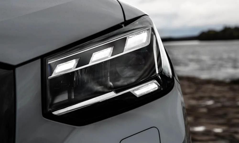 Фото Audi Q2 — вид спереди, фото 5. Серый кузов, строгая симметрия оптики — базовый ракурс знакомства с дизайном. Рисунок ходовых огней — подпись модели, по нему её узнают в потоке Audi Q2 — вид спереди, фото 5