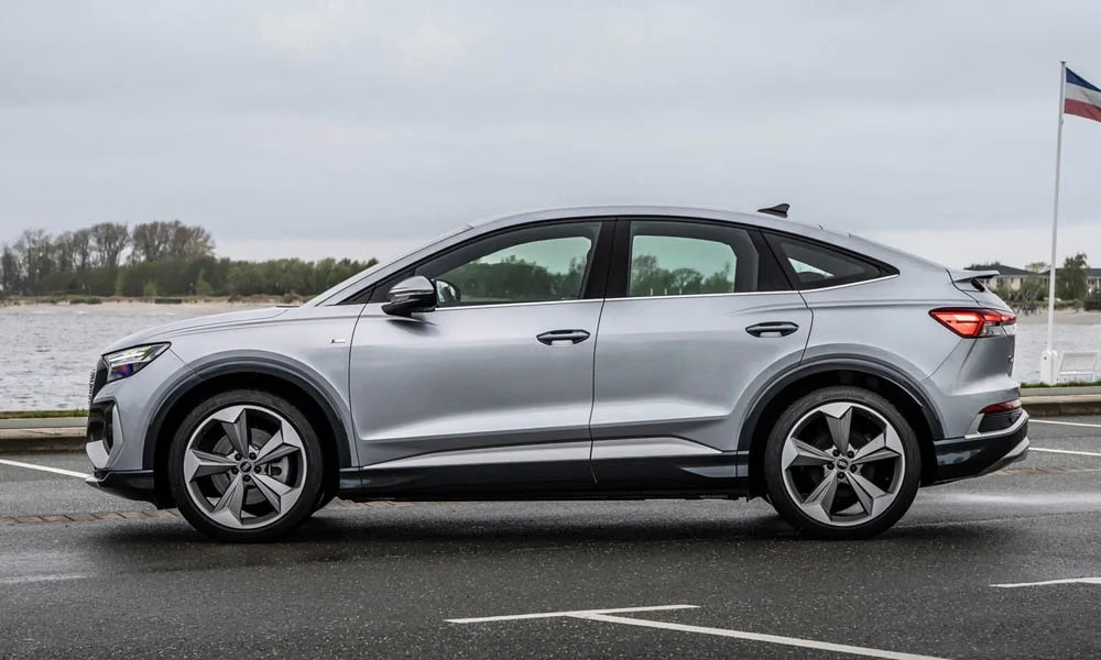 Фото Audi Q4 e-tron Sportback (2024) — вид сбоку, фото 3. Сбоку читаются линия остекления и характер выштамповок на серебристом кузове. Длинная база — простор второго ряда; короткие свесы упрощают парковку Audi Q4 e-tron Sportback (2024) — вид сбоку, фото 3