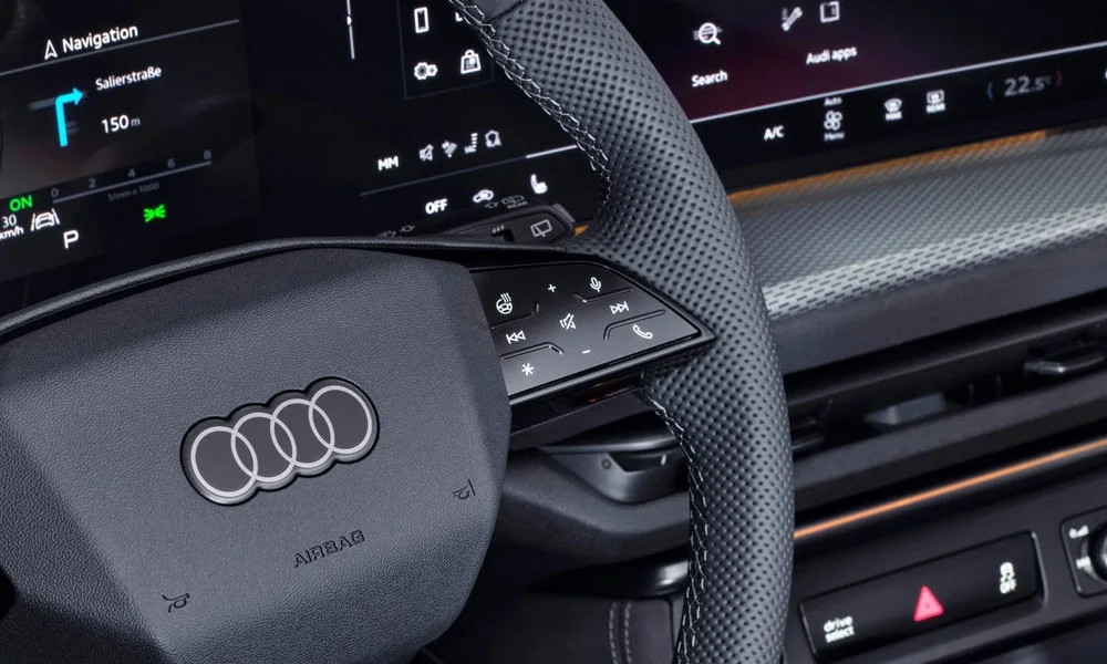 Фото Audi Q5 (2024) — руль. Обшивка обода и компоновка спиц крупным планом. Правильная посадка: руки на «9 и 3», приборы читаются поверх обода Audi Q5 (2024) — руль