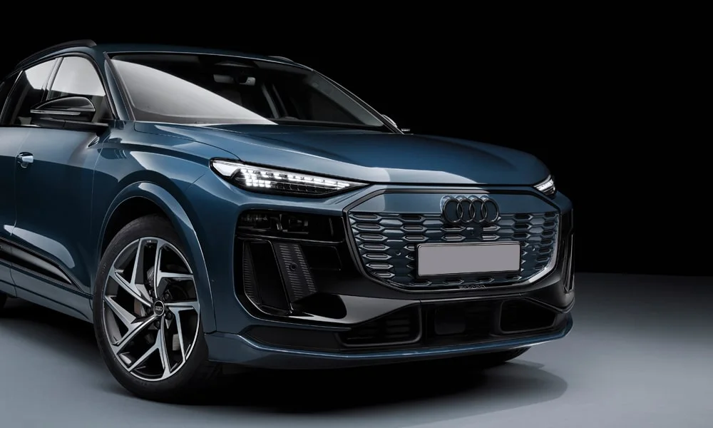 Фото Audi Q6 e-tron (2024) — вид спереди, фото 11. Синий кузов, строгая симметрия оптики — базовый ракурс знакомства с дизайном. Рисунок ходовых огней — подпись модели, по нему её узнают в потоке Audi Q6 e-tron (2024) — вид спереди, фото 11