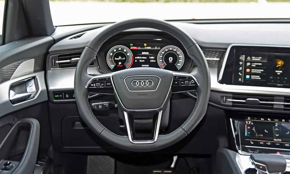 Фото Audi Q6 (2024) — руль. Обшивка обода и компоновка спиц крупным планом. Клавиши на спицах управляют медиа, круизом и ассистентами — руки остаются на руле Audi Q6 (2024) — руль