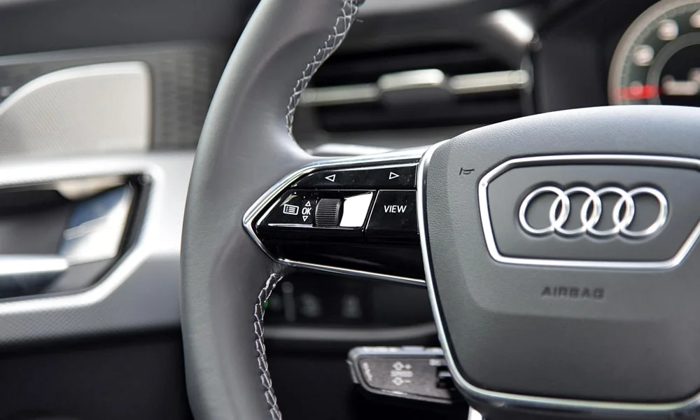 Фото Audi Q6 (2024) — руль, фото 2. Обшивка обода и компоновка спиц крупным планом. Клавиши на спицах управляют медиа, круизом и ассистентами — руки остаются на руле Audi Q6 (2024) — руль, фото 2