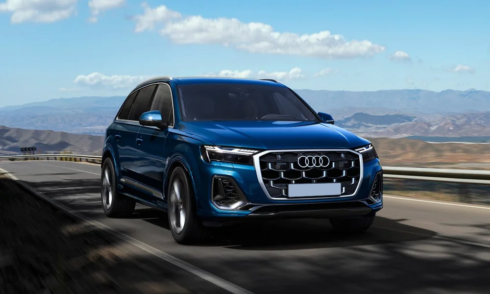 Фото Audi Q7 (2024) — вид спереди, фото 6. Кузов в синем цвете: рисунок оптики и решётки задаёт узнаваемое «лицо» модели. Рисунок ходовых огней — подпись модели, по нему её узнают в потоке Audi Q7 (2024) — вид спереди, фото 6
