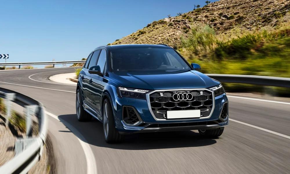 Фото Audi Q7 (2024) — вид спереди, фото 8. Синий кузов, строгая симметрия оптики — базовый ракурс знакомства с дизайном. Дневные ходовые огни включаются автоматически с запуском Audi Q7 (2024) — вид спереди, фото 8