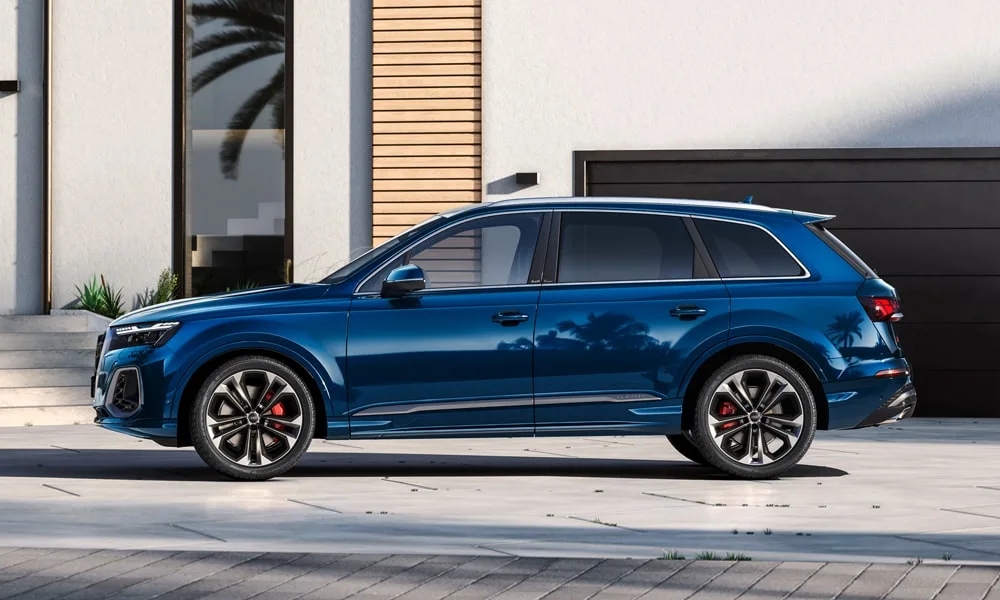 Фото Audi Q7 (2024) — вид сбоку, фото 3. Сбоку читаются линия остекления и характер выштамповок на синем кузове. Длинная база — простор второго ряда; короткие свесы упрощают парковку Audi Q7 (2024) — вид сбоку, фото 3