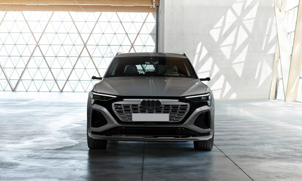 Фото Audi Q8 e-tron (2024) — вид спереди, фото 7. Кузов в сером цвете: рисунок оптики и решётки задаёт узнаваемое «лицо» модели Audi Q8 e-tron (2024) — вид спереди, фото 7