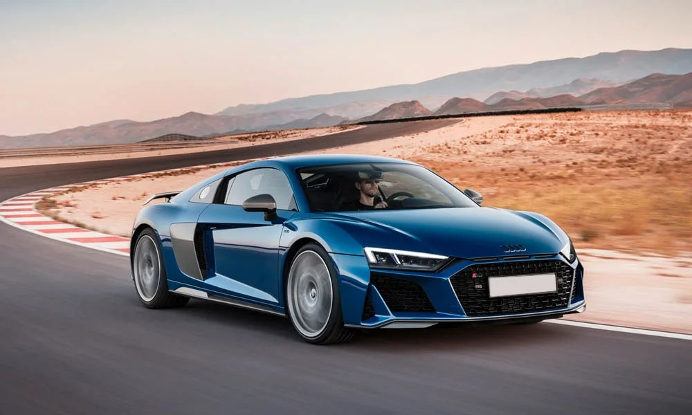 Фото Audi R8 (2024) — вид спереди, фото 7. Синий кузов, строгая симметрия оптики — базовый ракурс знакомства с дизайном. Рисунок ходовых огней — подпись модели, по нему её узнают в потоке Audi R8 (2024) — вид спереди, фото 7