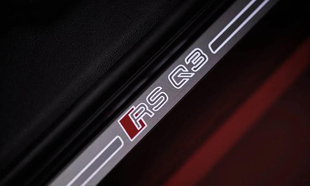 Фото Audi RS Q3 Sportback (2024) — дверная карта, фото 2. Дверная карта в красно-чёрной отделке: подлокотник, динамик и блок стеклоподъёмников. Решётка динамика в двери — часть штатной акустики Audi RS Q3 Sportback (2024) — дверная карта, фото 2