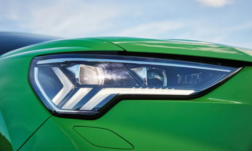 Фото Audi RS Q3 Sportback (2024) — вид спереди, фото 9. Кузов в зелёном цвете: рисунок оптики и решётки задаёт узнаваемое «лицо» модели. Рисунок ходовых огней — подпись модели, по нему её узнают в потоке Audi RS Q3 Sportback (2024) — вид спереди, фото 9