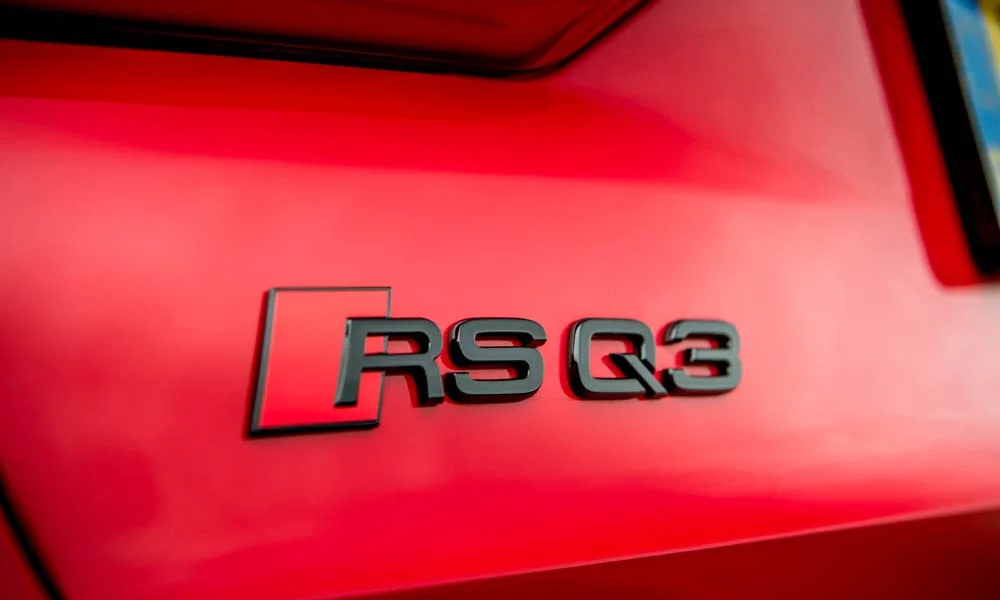 Фото Audi RS Q3 (2024) — эмблема. Логотип марки крупным планом. Шильдик версии на корме помогает отличать комплектации Audi RS Q3 (2024) — эмблема