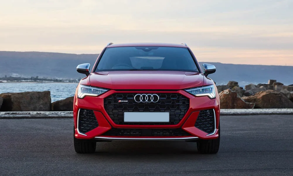 Фото Audi RS Q3 (2024) — вид спереди, фото 3. Кузов в красном цвете: рисунок оптики и решётки задаёт узнаваемое «лицо» модели. Рисунок ходовых огней — подпись модели, по нему её узнают в потоке Audi RS Q3 (2024) — вид спереди, фото 3