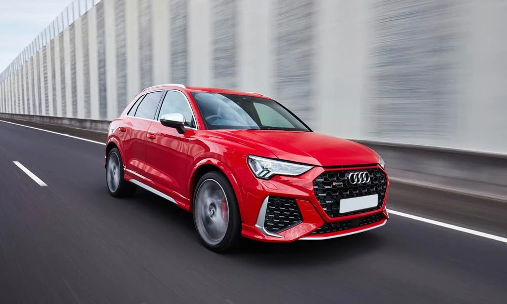 Фото Audi RS Q3 (2024) — вид спереди, фото 4. Кузов в красном цвете: рисунок оптики и решётки задаёт узнаваемое «лицо» модели. Рисунок ходовых огней — подпись модели, по нему её узнают в потоке Audi RS Q3 (2024) — вид спереди, фото 4