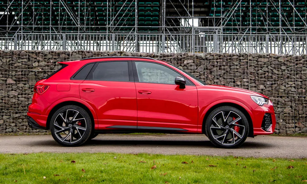 Фото Audi RS Q3 (2024) — вид сбоку, фото 2. Сбоку читаются линия остекления и характер выштамповок на красном кузове Audi RS Q3 (2024) — вид сбоку, фото 2