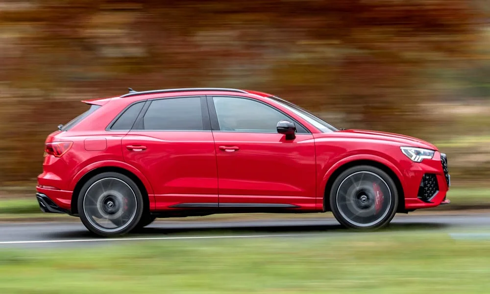 Фото Audi RS Q3 (2024) — вид сбоку, фото 4. Профиль в красном цвете: соотношение колёсной базы и свесов. Хромированные или чёрные молдинги окон отличают комплектации Audi RS Q3 (2024) — вид сбоку, фото 4