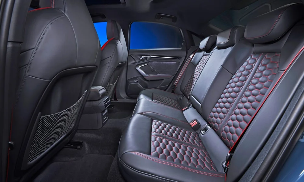 Фото Audi RS3 (2022) — задние сиденья. Задний диван в перфорированной коже: посадка и центральный подлокотник. Спинки складываются под длинные грузы у большинства версий Audi RS3 (2022) — задние сиденья