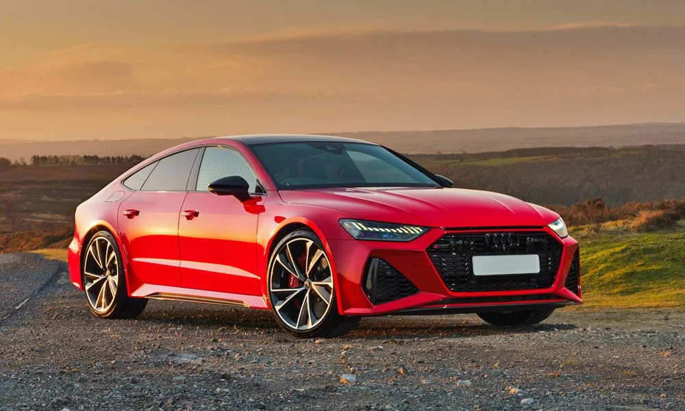 Фото Audi RS7 Sportback — вид спереди, фото 3. Кузов в красном цвете: рисунок оптики и решётки задаёт узнаваемое «лицо» модели. Дневные ходовые огни включаются автоматически с запуском Audi RS7 Sportback — вид спереди, фото 3