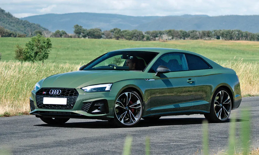 Фото Audi S5 (2024) — вид спереди, фото 16. Кузов в зелёном цвете: рисунок оптики и решётки задаёт узнаваемое «лицо» модели. Рисунок ходовых огней — подпись модели, по нему её узнают в потоке Audi S5 (2024) — вид спереди, фото 16