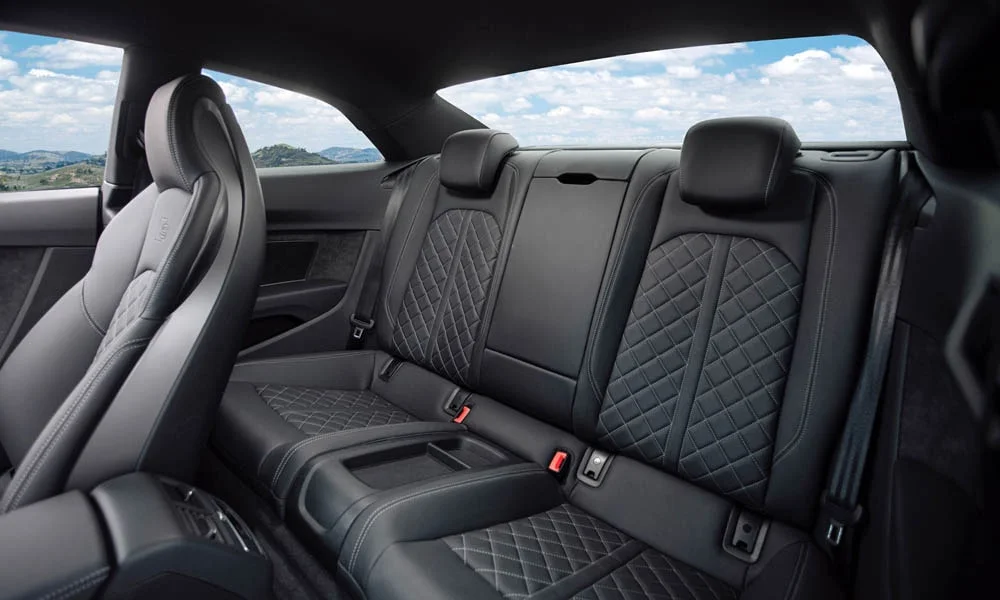 Фото Audi S5 (2024) — задние сиденья, фото 2. Посадка второго ряда: подголовники и подлокотник. Плоский пол упрощает посадку втроём Audi S5 (2024) — задние сиденья, фото 2