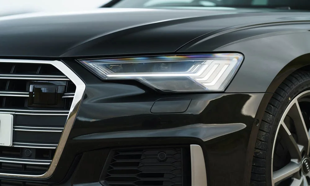 Фото Audi S6 Avant (2024) — вид спереди, фото 6. Кузов в чёрном цвете: рисунок оптики и решётки задаёт узнаваемое «лицо» модели. Дневные ходовые огни включаются автоматически с запуском Audi S6 Avant (2024) — вид спереди, фото 6