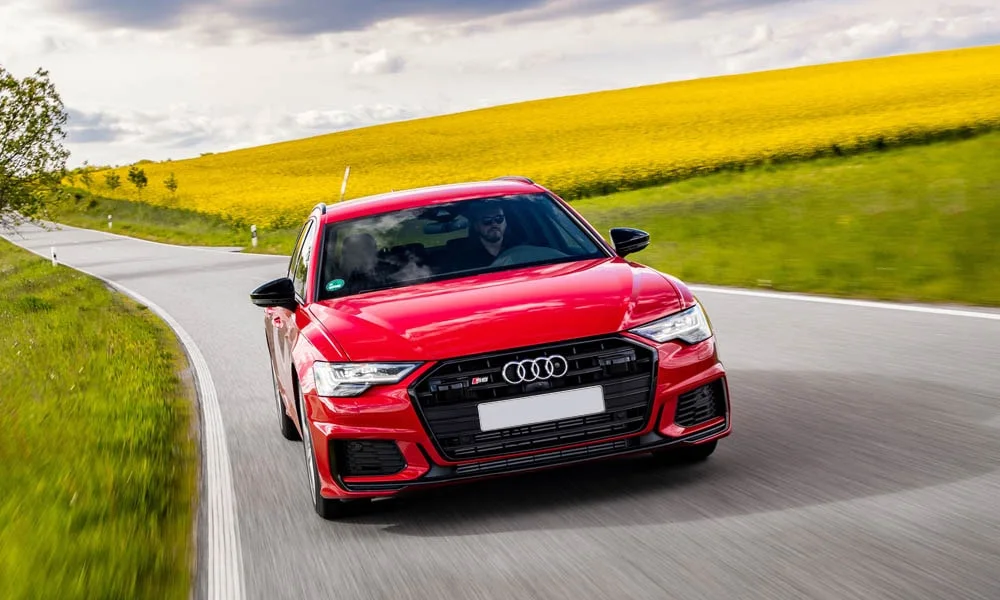 Фото Audi S6 Avant (2024) — вид спереди, фото 11. Красный кузов, строгая симметрия оптики — базовый ракурс знакомства с дизайном. Рисунок ходовых огней — подпись модели, по нему её узнают в потоке Audi S6 Avant (2024) — вид спереди, фото 11