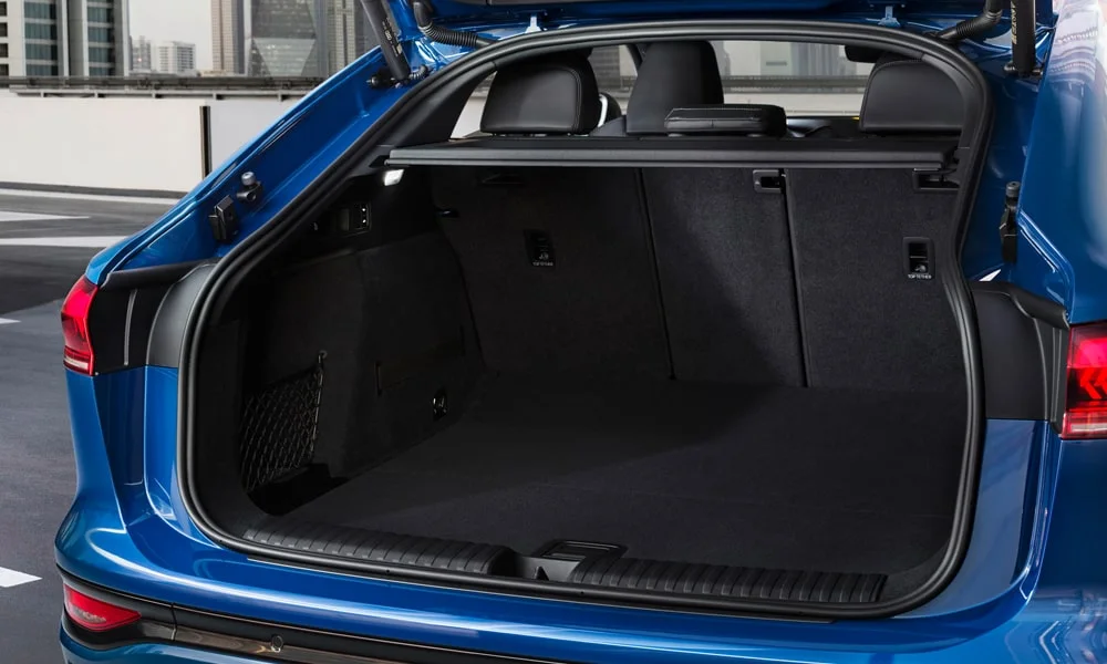 Фото Audi SQ6 Sportback e-tron (2024) — багажник. Форма проёма, ровный пол и организация пространства. Электропривод двери с датчиком под бампером — руки заняты, багажник открыт Audi SQ6 Sportback e-tron (2024) — багажник