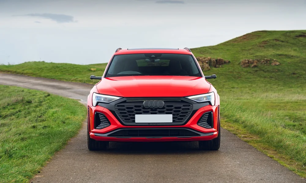 Фото Audi SQ8 e-tron — вид спереди, фото 3. Красный кузов, строгая симметрия оптики — базовый ракурс знакомства с дизайном. Дневные ходовые огни включаются автоматически с запуском Audi SQ8 e-tron — вид спереди, фото 3