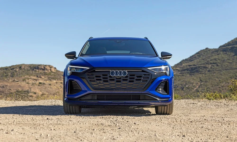 Фото Audi SQ8 e-tron — вид спереди, фото 6. Кузов в синем цвете: рисунок оптики и решётки задаёт узнаваемое «лицо» модели. Рисунок ходовых огней — подпись модели, по нему её узнают в потоке Audi SQ8 e-tron — вид спереди, фото 6
