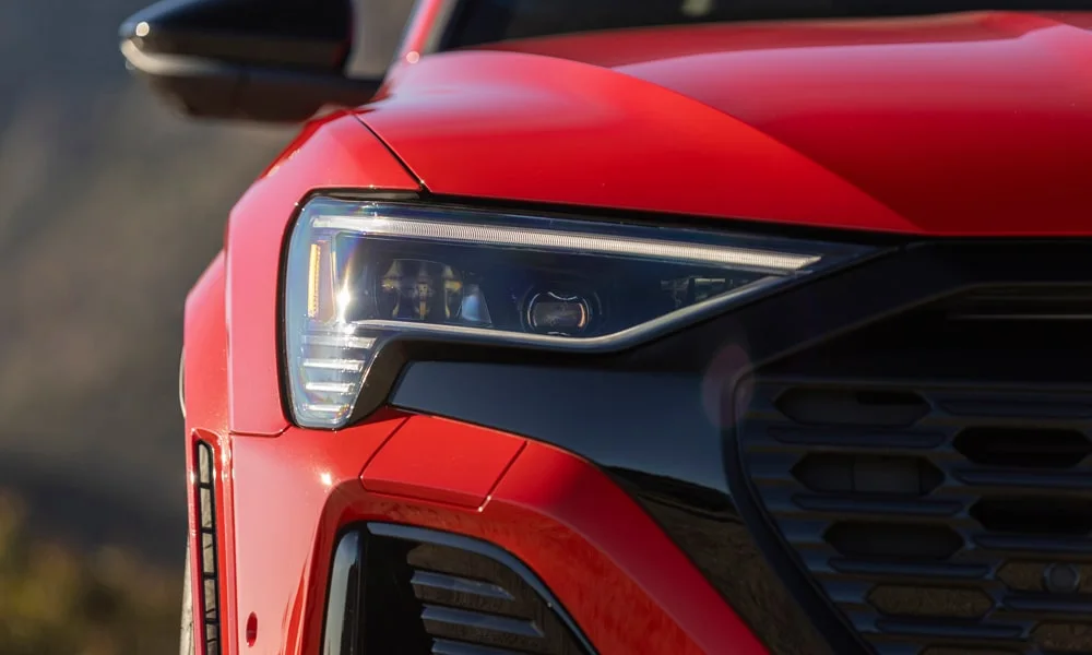 Фото Audi SQ8 Sportback e-tron (2024) — вид спереди, фото 5. Красный кузов, строгая симметрия оптики — базовый ракурс знакомства с дизайном. Рисунок ходовых огней — подпись модели, по нему её узнают в потоке Audi SQ8 Sportback e-tron (2024) — вид спереди, фото 5