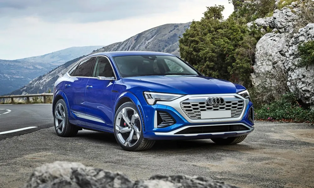 Фото Audi SQ8 Sportback e-tron (2024) — вид спереди, фото 6. Кузов в синем цвете: рисунок оптики и решётки задаёт узнаваемое «лицо» модели. Дневные ходовые огни включаются автоматически с запуском Audi SQ8 Sportback e-tron (2024) — вид спереди, фото 6