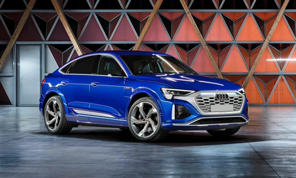 Фото Audi SQ8 Sportback e-tron (2024) — вид спереди, фото 12. Передок в синем исполнении — крупная светотехника и выразительный бампер. Рисунок ходовых огней — подпись модели, по нему её узнают в потоке Audi SQ8 Sportback e-tron (2024) — вид спереди, фото 12