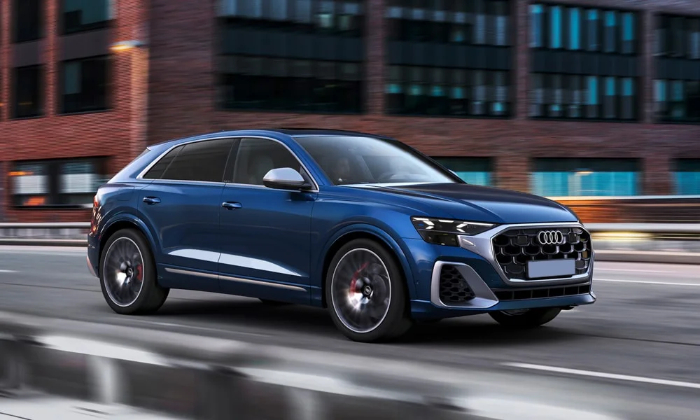 Фото Audi SQ8 (2024) — вид спереди, фото 4. Синий кузов, строгая симметрия оптики — базовый ракурс знакомства с дизайном. Рисунок ходовых огней — подпись модели, по нему её узнают в потоке Audi SQ8 (2024) — вид спереди, фото 4