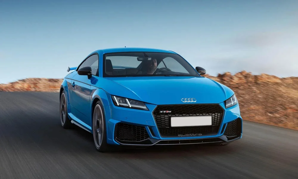 Фото Audi TT RS — вид спереди, фото 4. Кузов в синем цвете: рисунок оптики и решётки задаёт узнаваемое «лицо» модели. Рисунок ходовых огней — подпись модели, по нему её узнают в потоке Audi TT RS — вид спереди, фото 4