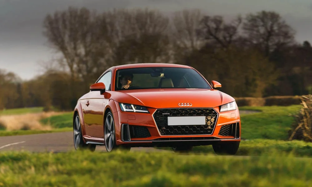 Фото Audi TT — вид спереди, фото 5. Оранжевый кузов, строгая симметрия оптики — базовый ракурс знакомства с дизайном. Дневные ходовые огни включаются автоматически с запуском Audi TT — вид спереди, фото 5