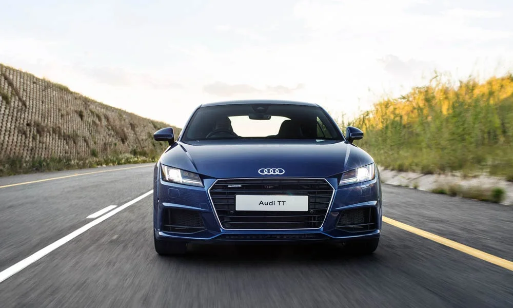 Фото Audi TT — вид спереди, фото 12. Кузов в синем цвете: рисунок оптики и решётки задаёт узнаваемое «лицо» модели. Рисунок ходовых огней — подпись модели, по нему её узнают в потоке Audi TT — вид спереди, фото 12