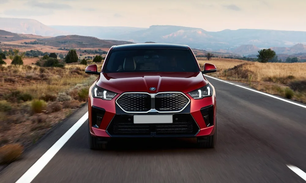 Фото BMW iX2 — вид спереди, фото 4. Передок в красном исполнении — крупная светотехника и выразительный бампер. Рисунок ходовых огней — подпись модели, по нему её узнают в потоке BMW iX2 — вид спереди, фото 4