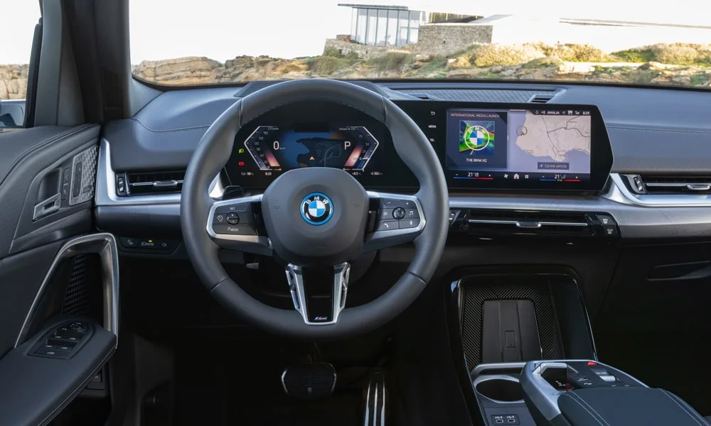 Фото BMW iX2 — руль. Обшивка обода и компоновка спиц крупным планом. Правильная посадка: руки на «9 и 3», приборы читаются поверх обода BMW iX2 — руль