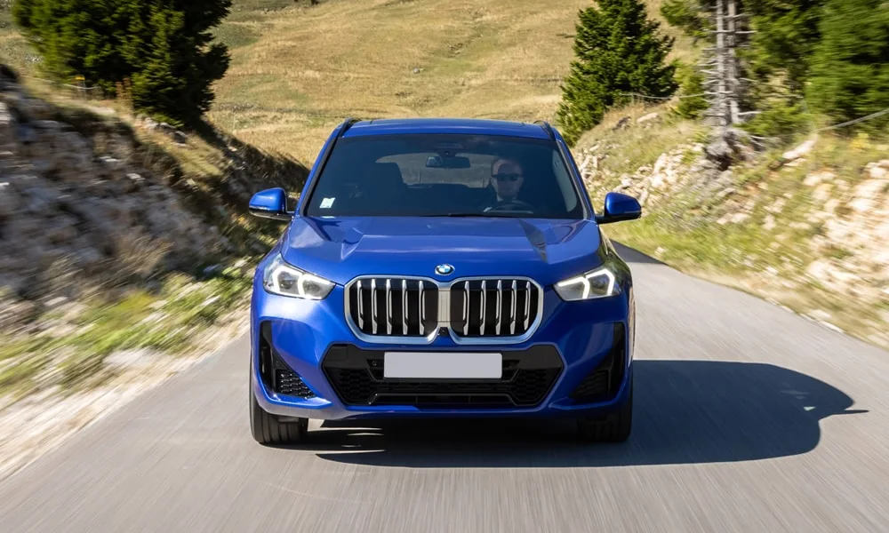 Фото BMW X1 (2024) — вид спереди, фото 5. Кузов в синем цвете: рисунок оптики и решётки задаёт узнаваемое «лицо» модели. Дневные ходовые огни включаются автоматически с запуском BMW X1 (2024) — вид спереди, фото 5