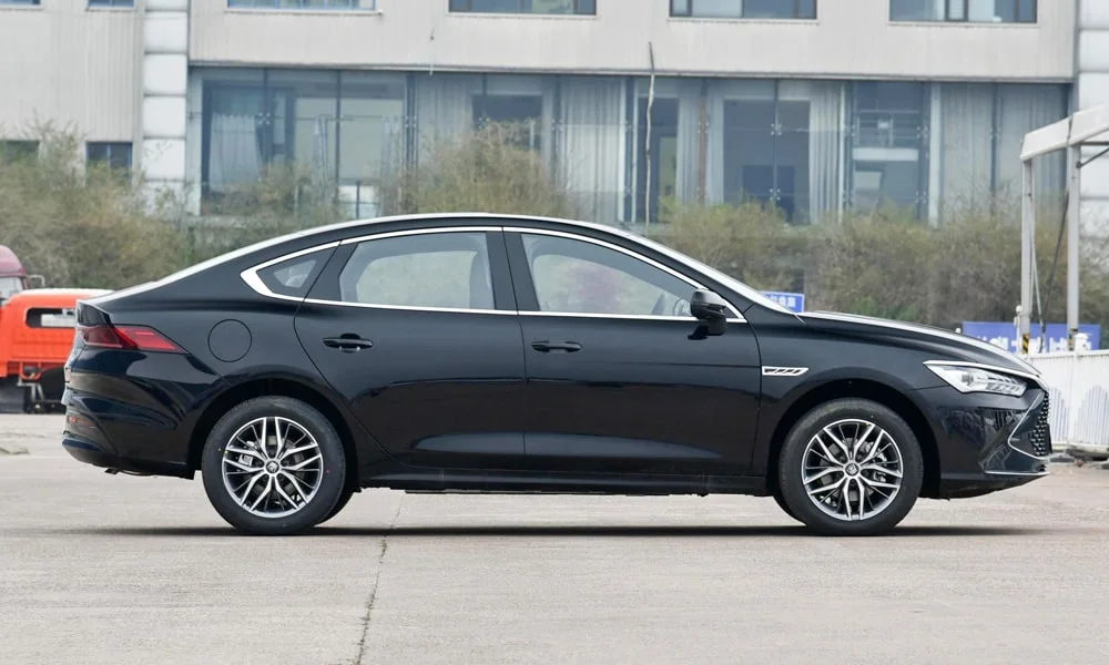 Фото BYD Qin Plus (2024) — вид сбоку, фото 3. Сбоку читаются линия остекления и характер выштамповок на чёрном кузове. Хромированные или чёрные молдинги окон отличают комплектации BYD Qin Plus (2024) — вид сбоку, фото 3