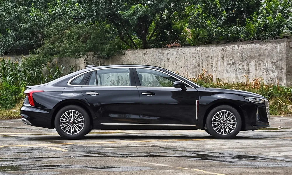 Фото Hongqi H5 (2023) — вид сбоку, фото 7. Сбоку читаются линия остекления и характер выштамповок на чёрном кузове. Хромированные или чёрные молдинги окон отличают комплектации Hongqi H5 (2023) — вид сбоку, фото 7