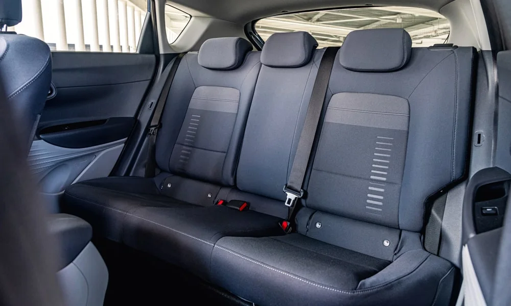 Фото Hyundai Bayon (2024) — задние сиденья. Задний диван в практичной ткани: посадка и центральный подлокотник. Спинки складываются под длинные грузы у большинства версий Hyundai Bayon (2024) — задние сиденья