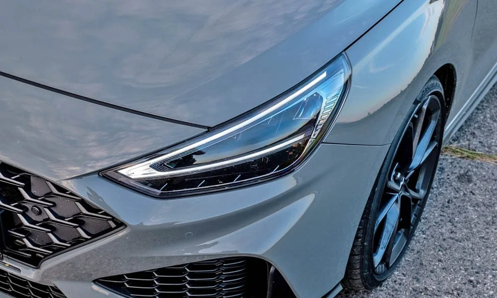 Фото Hyundai i30 Fastback N (2024) — вид спереди, фото 6. Серый кузов, строгая симметрия оптики — базовый ракурс знакомства с дизайном. Дневные ходовые огни включаются автоматически с запуском Hyundai i30 Fastback N (2024) — вид спереди, фото 6